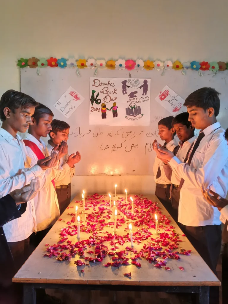 Students standing in silent prayer behind a table of candles on 16 December