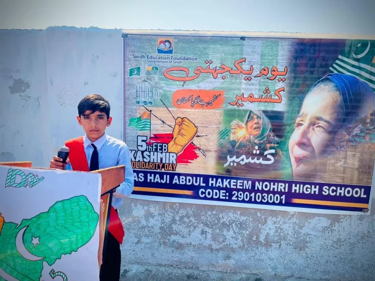 Student with a red sash speaking at the Kashmir Day programme