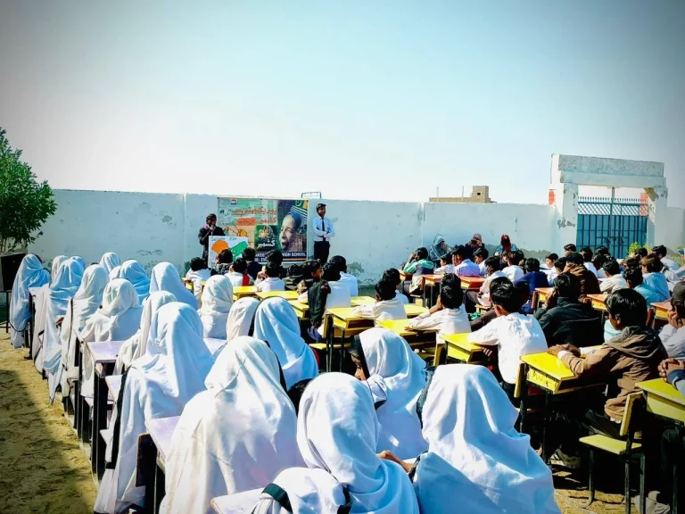 Girls and boys seated in the school ground listening to Kashmir Day speeches