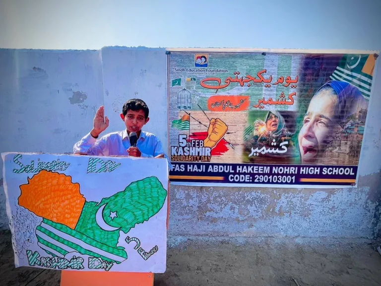 Student speaking at the podium with a Kashmir Solidarity Day banner behind him