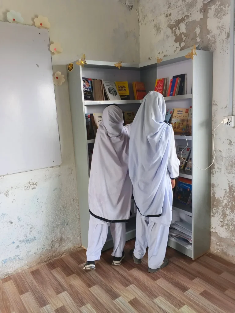 Two girls choosing books from the school library shelves