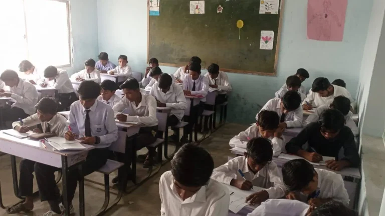 Boys in school uniform writing midterm examination papers at their desks